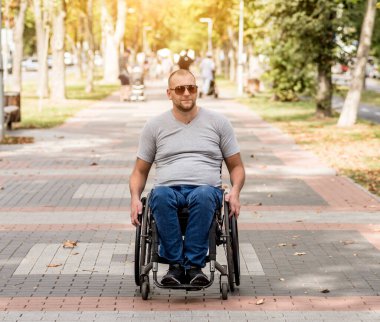 Tekerlekli sandalyedeki engelli adam parkta yürüyor.