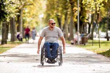 Tekerlekli sandalyedeki engelli adam parkta yürüyor.