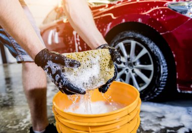 İşçi araba yıkamada kırmızı arabayı süngerle yıkıyor.