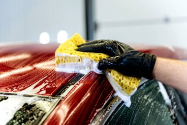 İşçi araba yıkamada kırmızı arabayı süngerle yıkıyor.