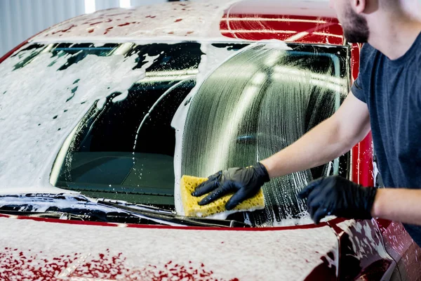 Trabajador lavando coche rojo con esponja en un lavado de coche — Foto de Stock