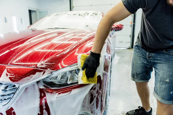 Trabajador lavando coche rojo con esponja en un lavado de coche — Foto de Stock