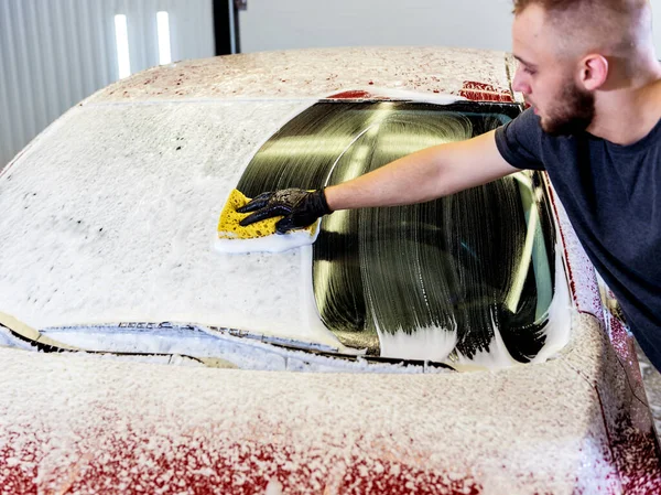 Trabajador lavando coche rojo con esponja en un lavado de coche — Foto de Stock