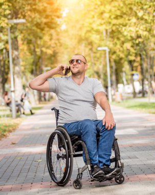 Park sokağındaki tekerlekli sandalyedeki engelli adam akıllı telefon kullanıyor.