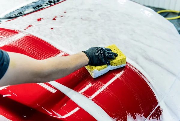 İşçi araba yıkamada kırmızı arabayı süngerle yıkıyor. — Stok fotoğraf