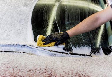 İşçi araba yıkamada kırmızı arabayı süngerle yıkıyor.