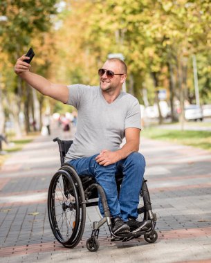 Park sokağındaki tekerlekli sandalyedeki engelli adam akıllı telefon kullanıyor.