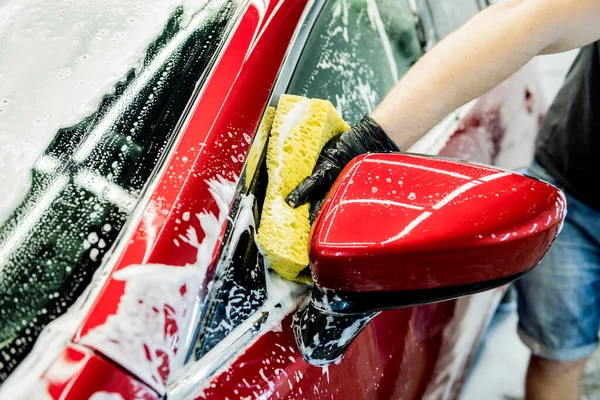 Trabajador lavando coche rojo con esponja en un lavado de coche — Foto de Stock