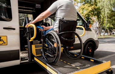 Tekerlekli sandalyedeki bir adam engelliler için araç kaldırıyor.