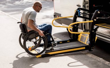 Tekerlekli sandalyedeki bir adam özel bir aracın asansörüne biner. 