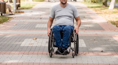 Tekerlekli sandalyedeki engelli adam parkta yürüyor.