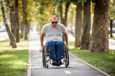Tekerlekli sandalyedeki engelli adam parkta yürüyor.