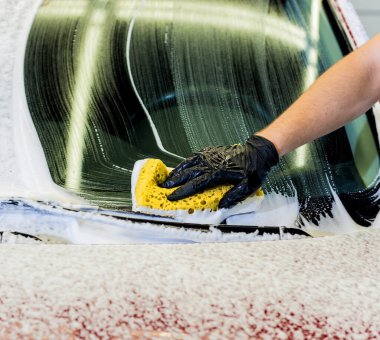 İşçi araba yıkamada kırmızı arabayı süngerle yıkıyor.