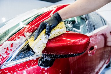 İşçi araba yıkamada kırmızı arabayı süngerle yıkıyor.