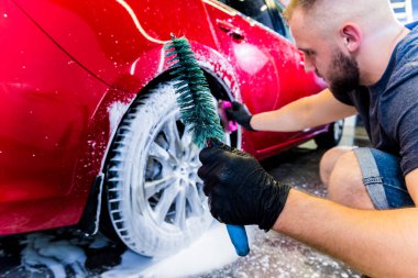 Araba tekerleğini fırça ve suyla temizliyorum.