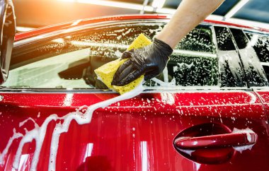 İşçi araba yıkamada kırmızı arabayı süngerle yıkıyor.