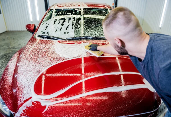 Trabajador lavando coche rojo con esponja en un lavado de coche —  Fotos de Stock