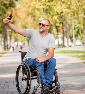 Park sokağındaki tekerlekli sandalyedeki engelli adam akıllı telefon kullanıyor.