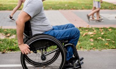 Tekerlekli sandalyedeki engelli adam parkta yürüyor.