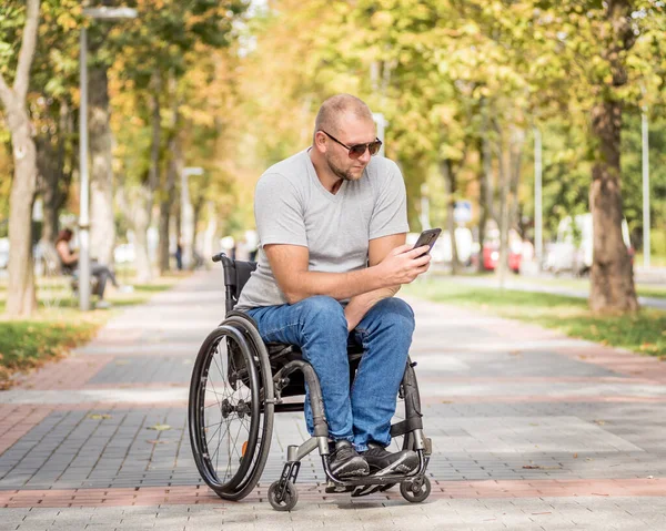 Handicapped man in wheelchair at the park alley use a smartphone