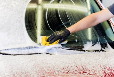 İşçi araba yıkamada kırmızı arabayı süngerle yıkıyor.