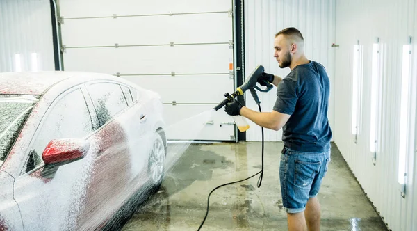 Trabajador de lavado de coches con agua de alta presión en un lavado de coches. — Foto de Stock