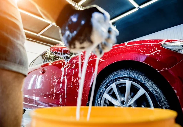Ouvrier laver voiture rouge avec éponge sur un lavage de voiture — Photo