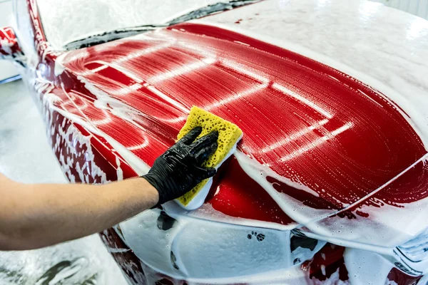 Trabajador lavando coche rojo con esponja en un lavado de coche — Foto de Stock