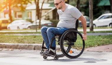 Tekerlekli sandalyedeki engelli adam caddeden karşıya geçiyor.