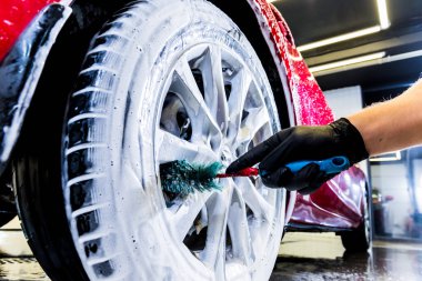 Araba tekerleğini fırça ve suyla temizliyorum.