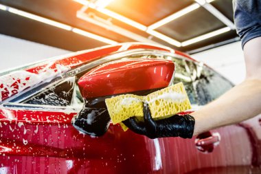 İşçi araba yıkamada kırmızı arabayı süngerle yıkıyor.