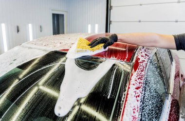 İşçi araba yıkamada kırmızı arabayı süngerle yıkıyor.