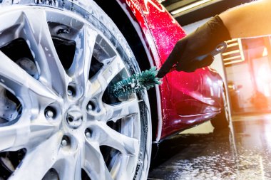 Araba tekerleğini fırça ve suyla temizliyorum.