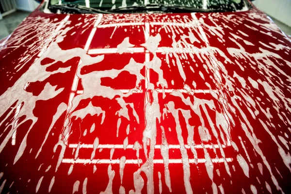 자동차 세차장에서 거품을 발린 붉은 차를 씻는 모습. — 스톡 사진
