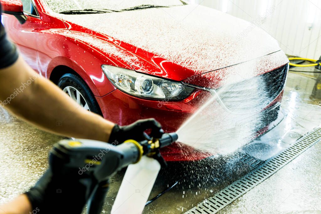 Worker washing car with active foam on a car wash.