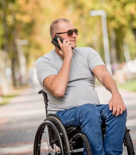 Handicapped man in wheelchair at the park alley use a smartphone