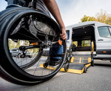 Tekerlekli sandalyedeki bir adam özel bir aracın asansörüne biner. 