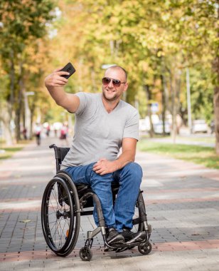 Park sokağındaki tekerlekli sandalyedeki engelli adam akıllı telefon kullanıyor.