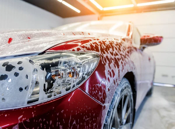 Mycie czerwonego samochodu z aktywną pianką w myjni samochodowej. — Zdjęcie stockowe