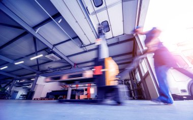 Depoda çalışan bir işçi paletleri taşımak için bir el paleti istifleyicisi kullanır..