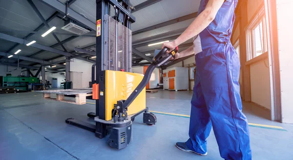 Een arbeider in een magazijn gebruikt een handpalletstapelaar om pallets te transporteren. — Stockfoto