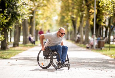 Tekerlekli sandalyedeki engelli adam parkta yürüyor.