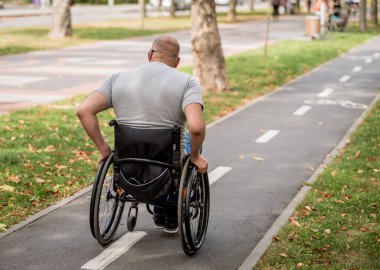 Handicapped man in wheelchair walk at the park alley clipart