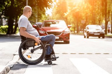 Tekerlekli sandalyedeki engelli adam caddeden karşıya geçiyor.