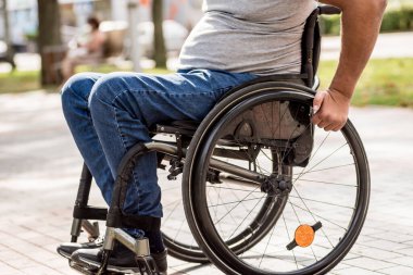 Tekerlekli sandalyedeki engelli adam parkta yürüyor.