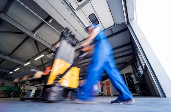 Um trabalhador em um armazém usa um empilhador de paletes de mão para transportar paletes. — Fotografia de Stock
