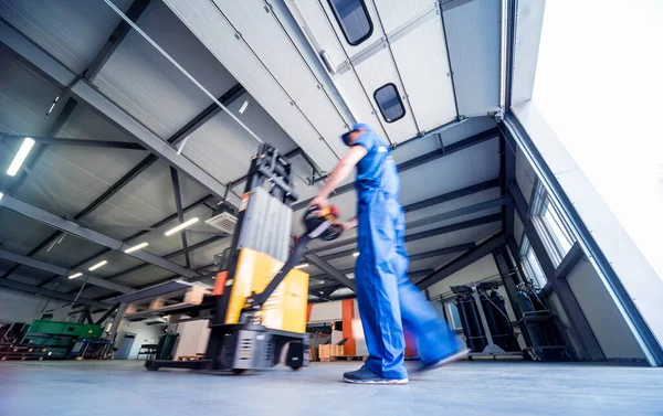 Um trabalhador em um armazém usa um empilhador de paletes de mão para transportar paletes. — Fotografia de Stock