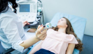 Doktor, bir kadının tiroidini incelemek için ultrason cihazı kullanıyor.