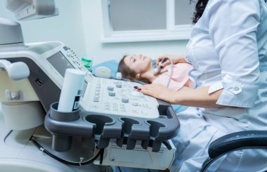 Doktor, bir kadının tiroidini incelemek için ultrason cihazı kullanıyor.