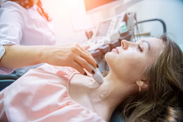 Doctor using ultrasound scanning machine for examining a thyroid of woman